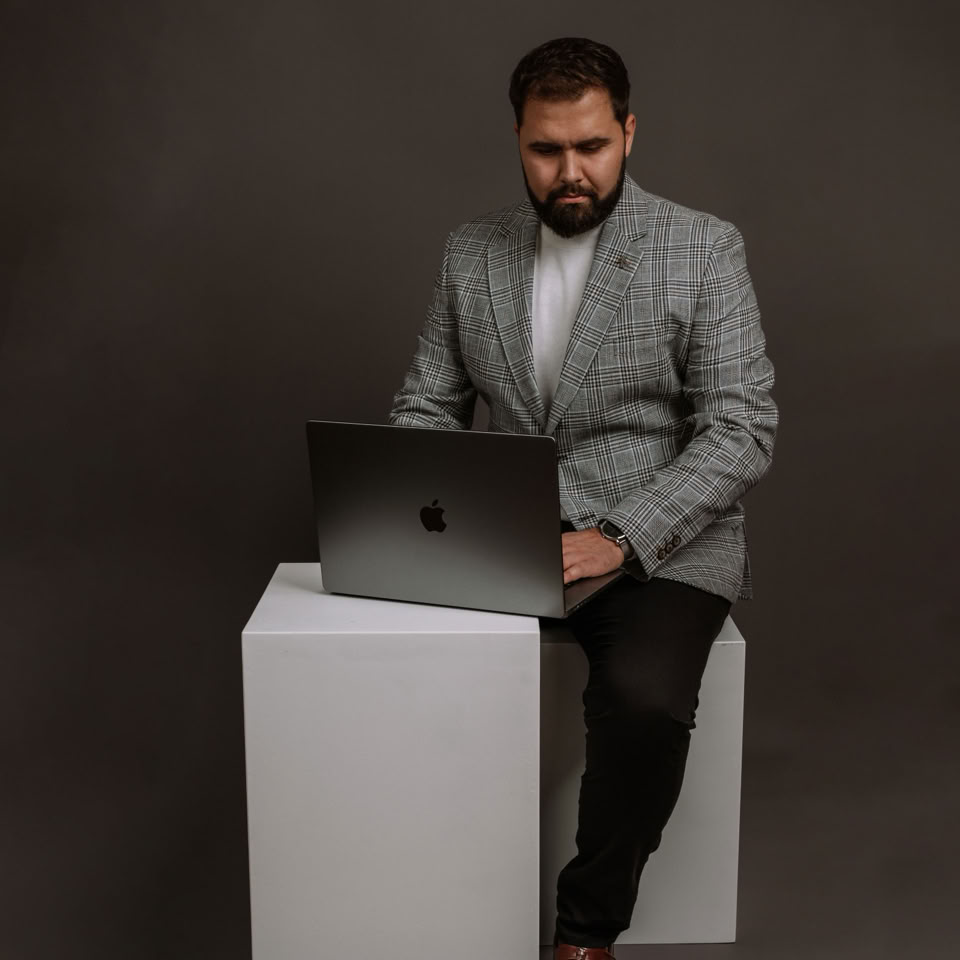 Confident businessman in grey suit works on laptop in a professional studio setting.
