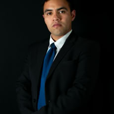 Professional portrait of a man in a suit and tie against a dark background.